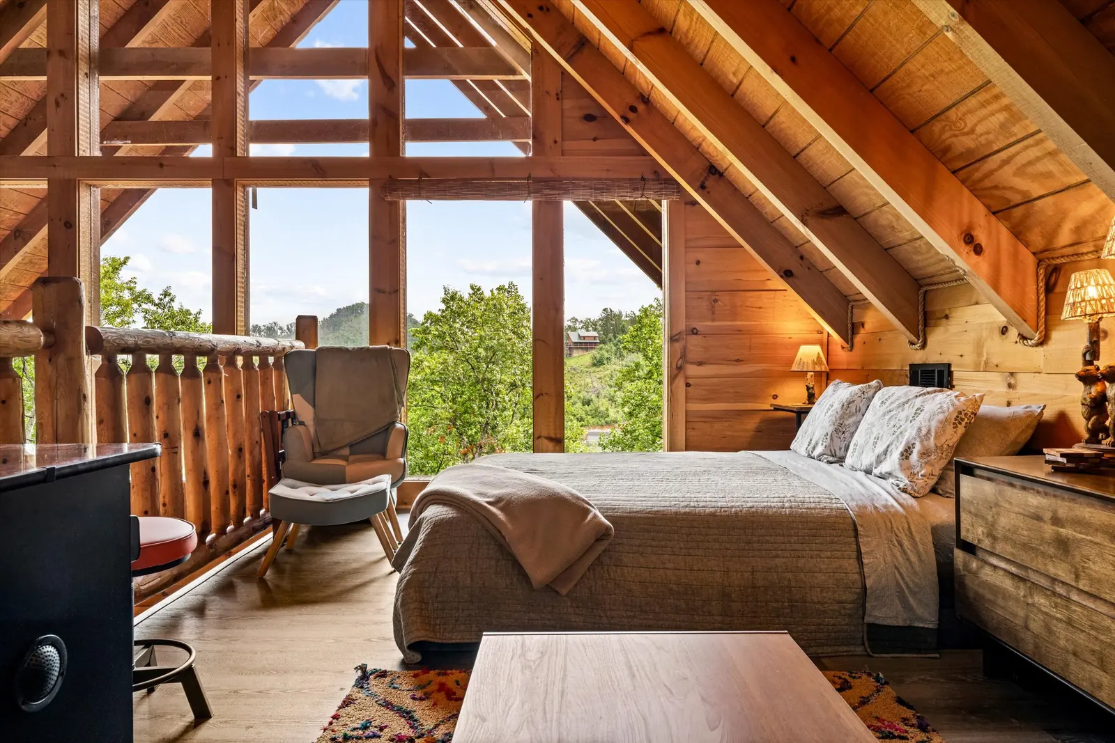 Queen bed in the open loft with a wall of windows and A-frame beams