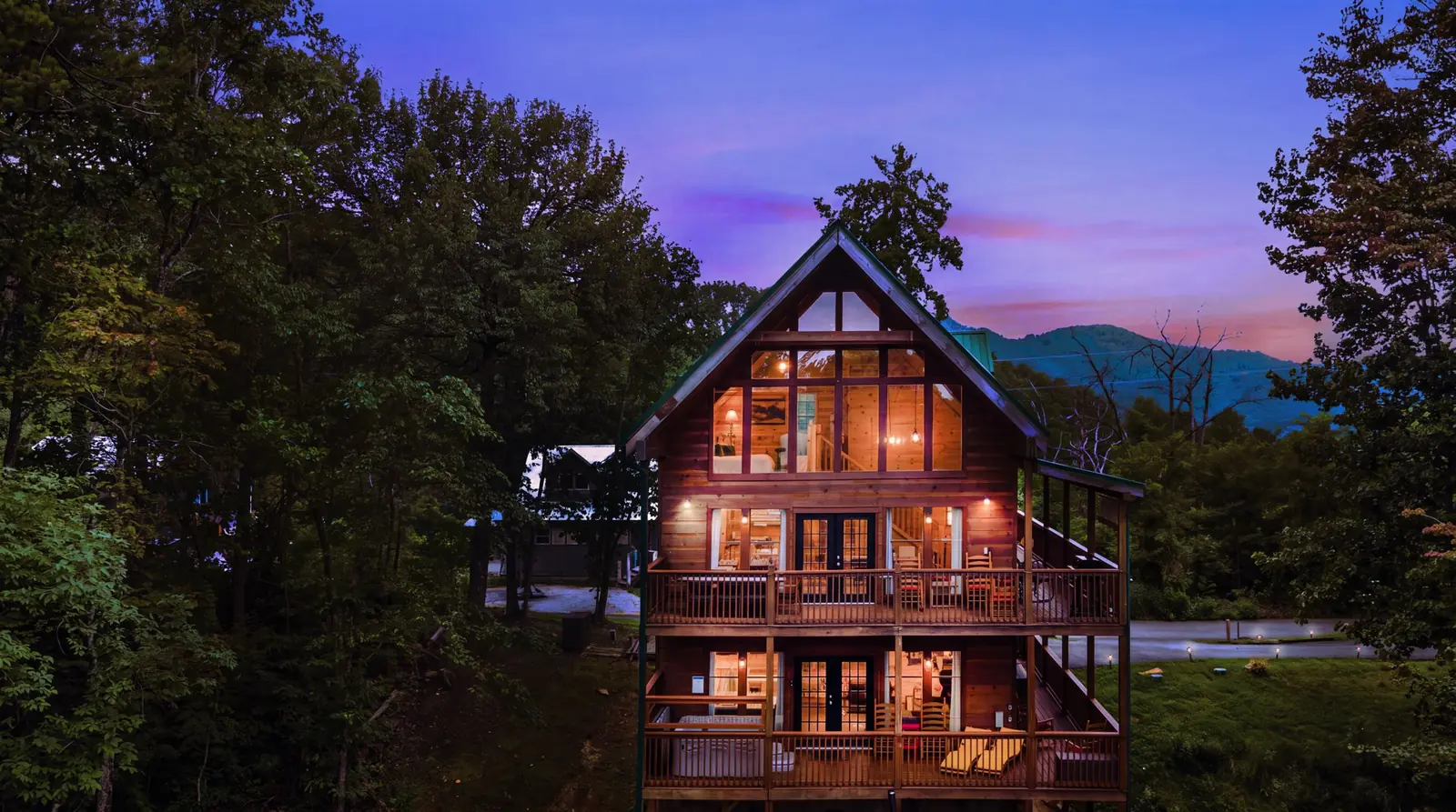 Acorn Ridge cabin lit from within at dusk, three stories of deck facing the Smoky Mountains